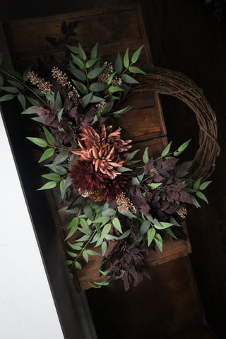 Decorative wreath with artificial flowers and leaves on a wooden surface