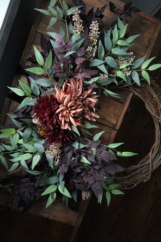 Decorative wreath with artificial leaves and flowers on a wooden surface