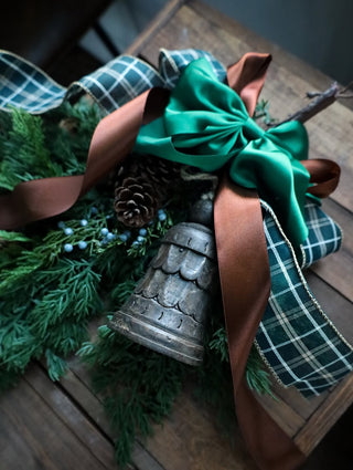Decorative wreath with greenery, pinecones, and ribbons on a wooden surface